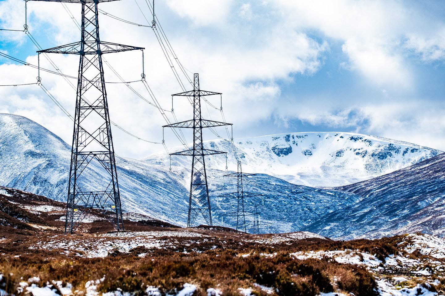 A series of transmission towers stand proudly across the Scottish Highlands against a snowy backdrop