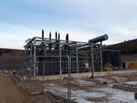 Black metal substation infrastructure, surrounded by a metal frame. A contractor in PPE stands atop the infrastructure.