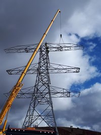 A three-directional metal transmission tower under construction.