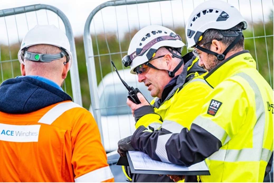 Engineers with contracting partners are working together, dressed in hi-vis jackets, making use of a walkie-talkie