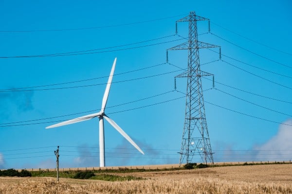 A wind turbine in the landscape alongside an electricity pylon