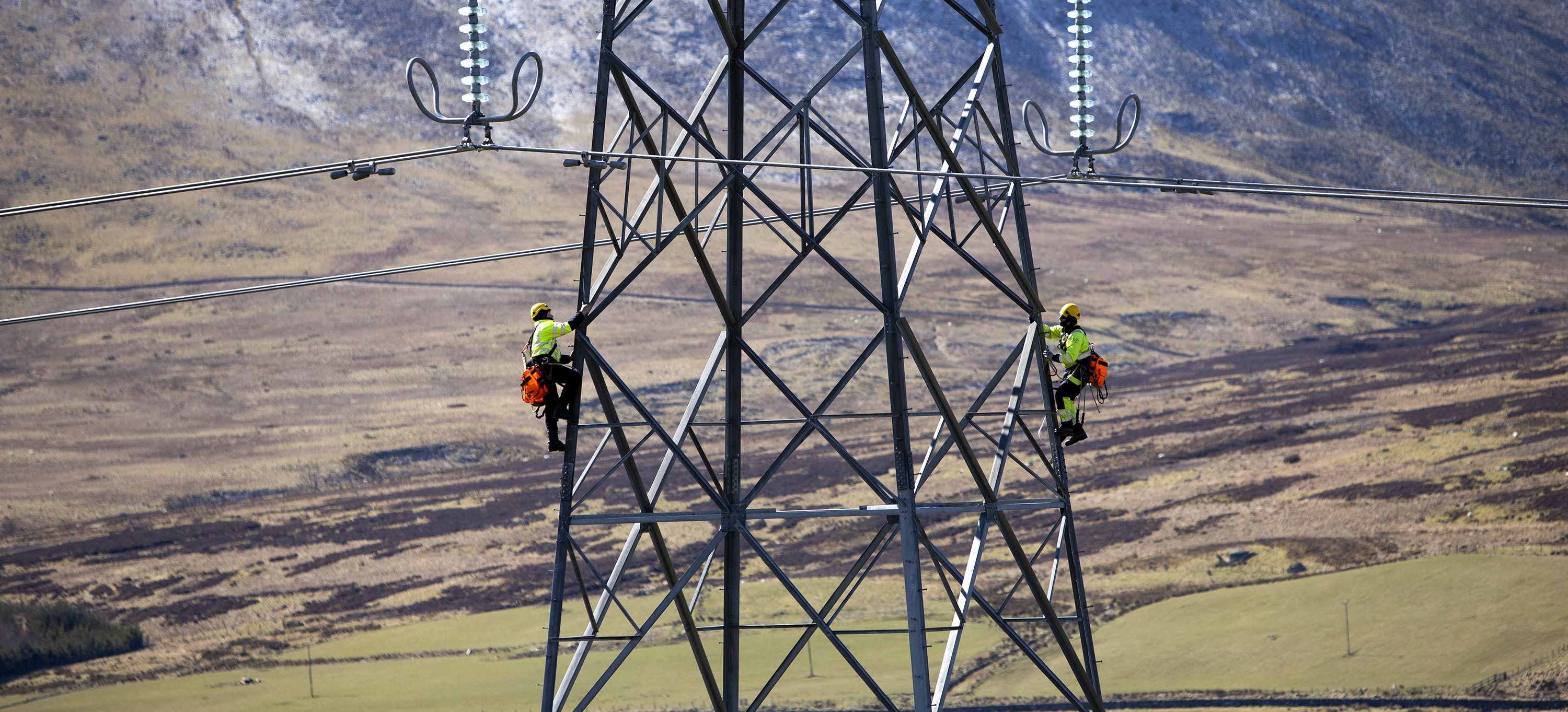 A closeup of a section of an electricity tower (pylon) with two maintenence workers climbing up each side