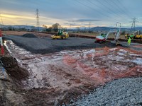 Construction vehicles surfacing a dirt area with a rocky surfacing material.