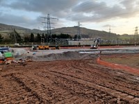 A dirt area next to a partially surfaced area using a rocky surfacing material. A substation is visible in the background.