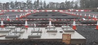 A concrete slab with fittings emerging from it, in the background there are several excavated sections of a construction site surrounded by traffic cones and construction barriers.