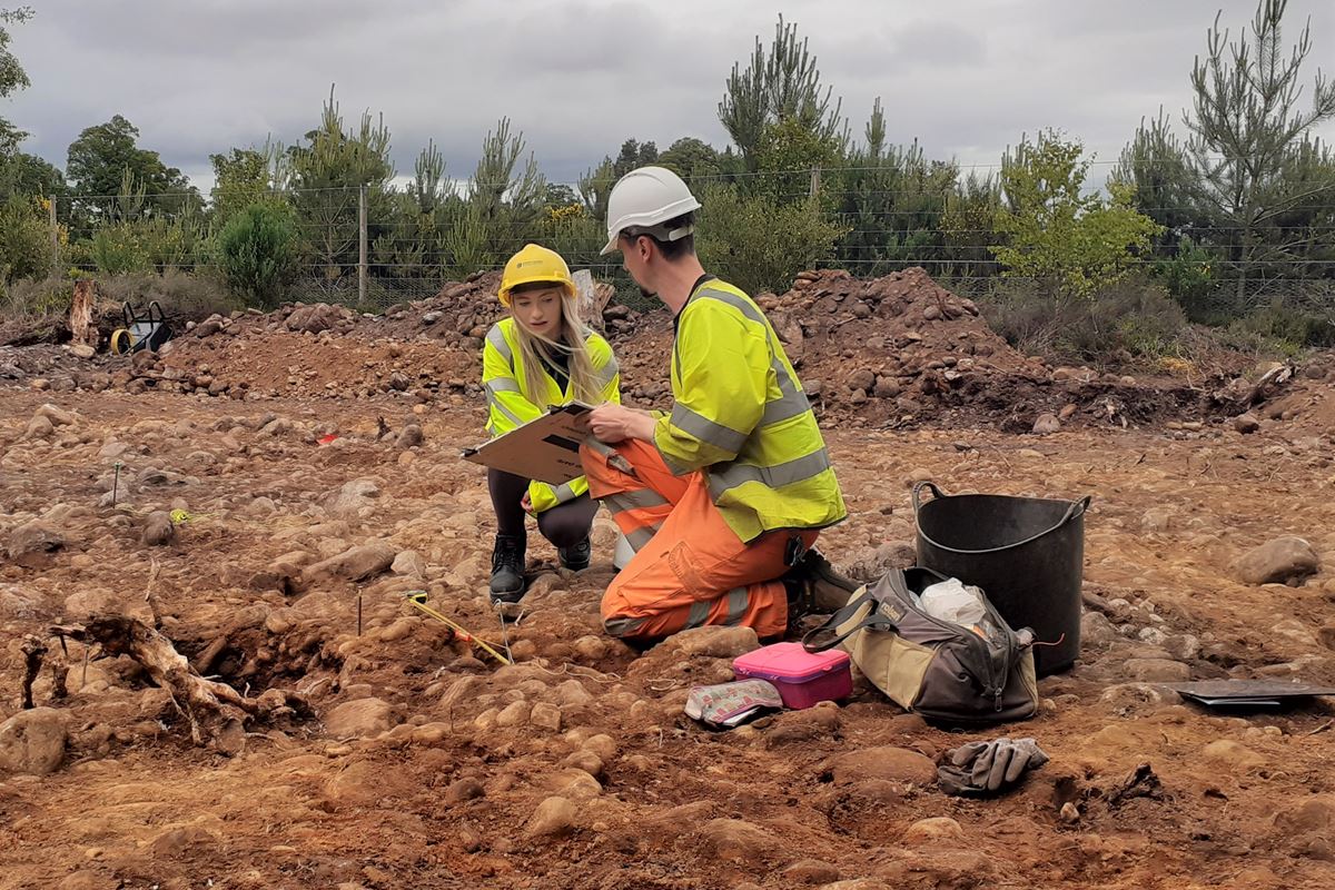 Archaeologists in PPE with artifacts in a stone dirt area.
