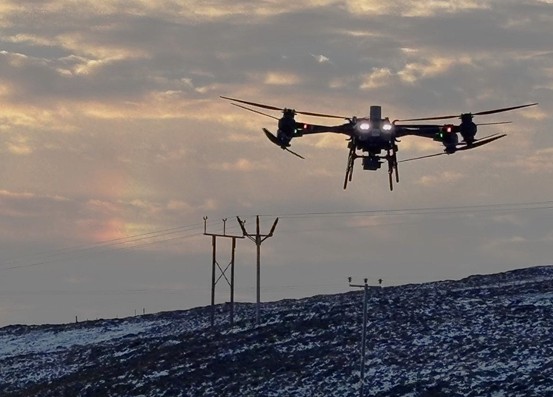 A heavy-lift DJI FlyCart 30 Drone in front of wooden pole transmission towers.