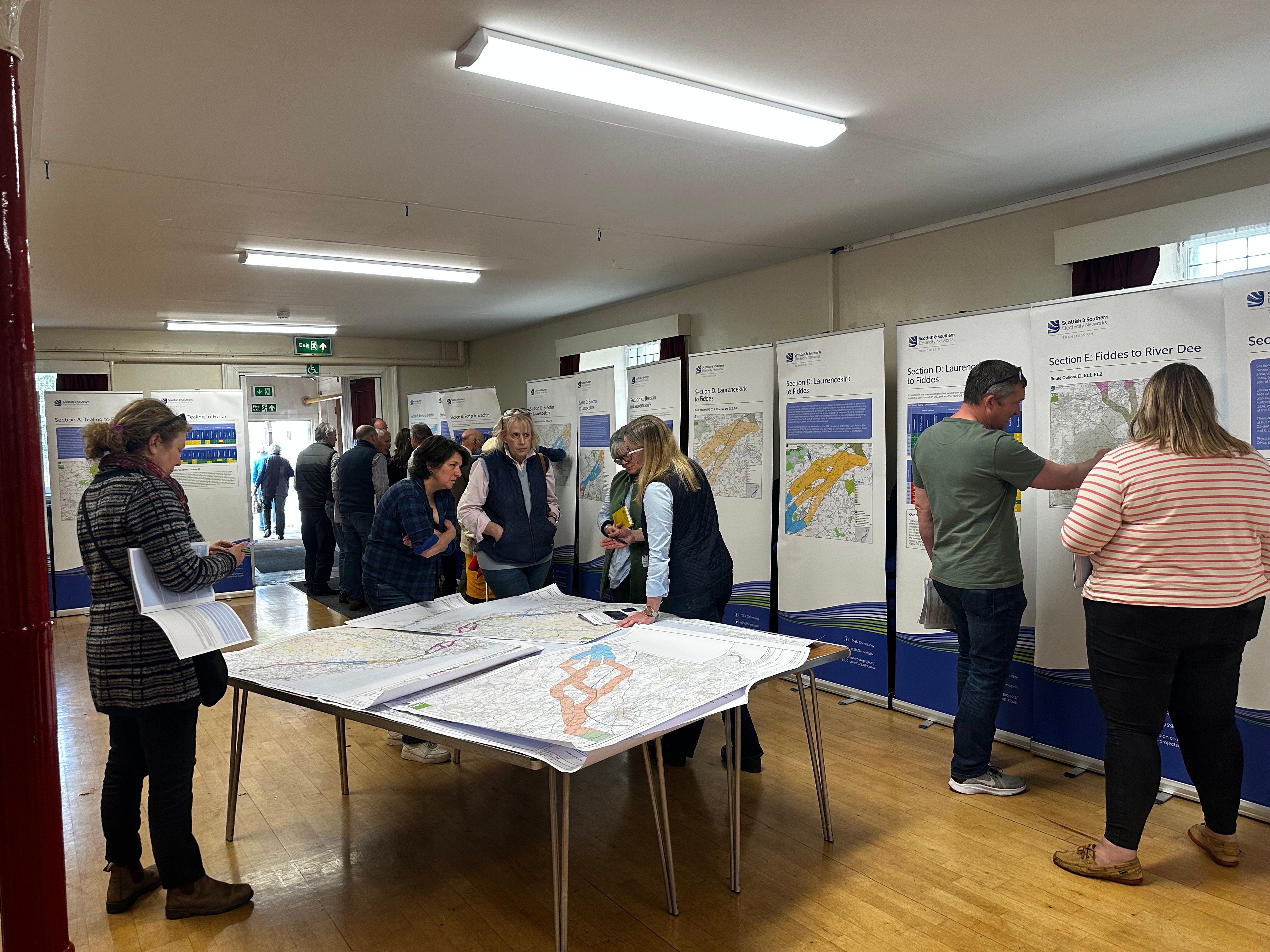 Members of the public and SSEN Transmission employees examining project posters in a hall.