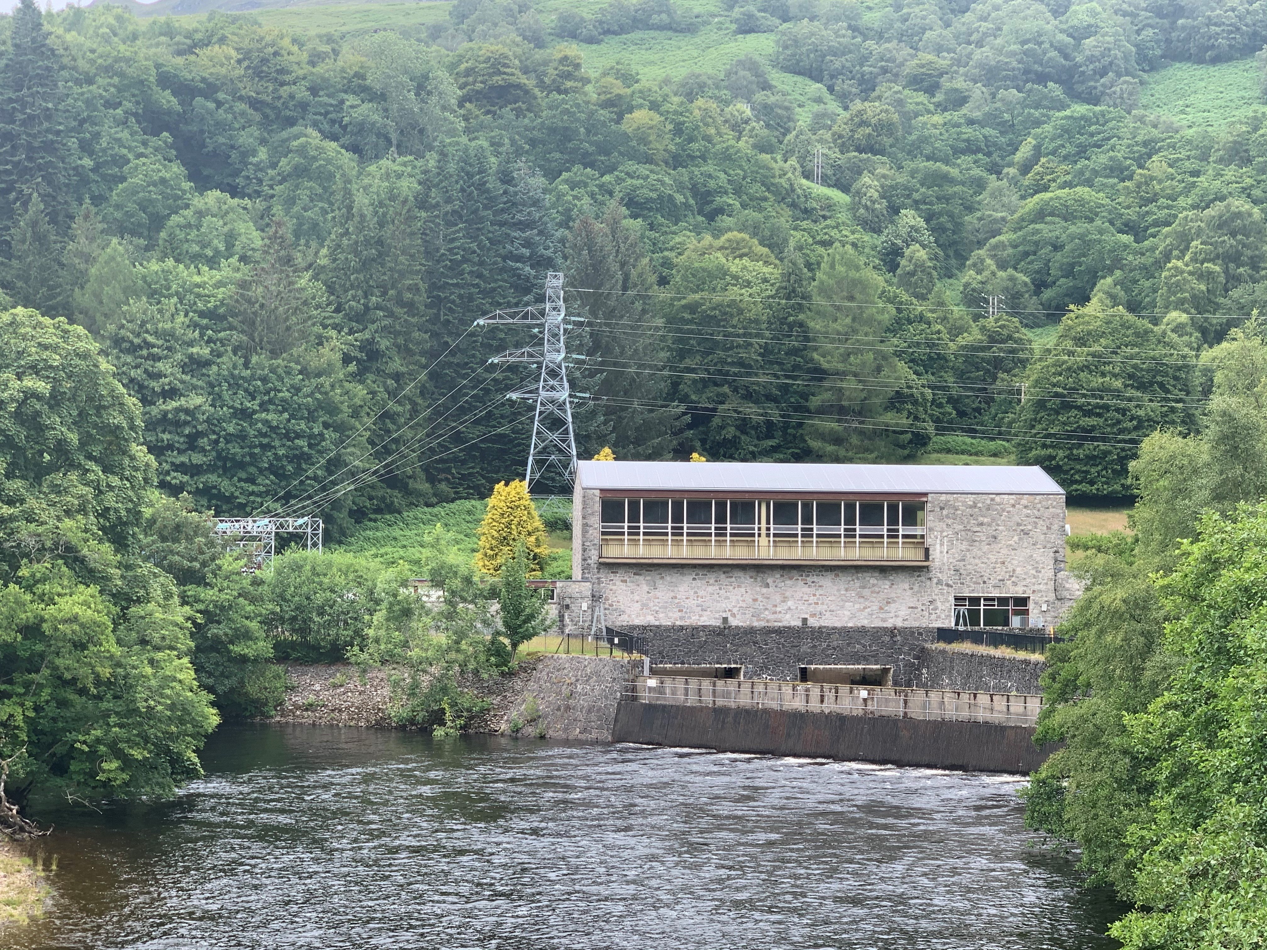 Power station showing substation A stone building, an overhead line leads into a courtyard obscured by trees.