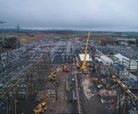 A wide aerial view of a substation, with a large crane and other construction vehicles in the foreground.