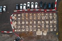 An overhead view of a dirt area on a construction site.  Concrete squares are placed at intervals across the area. Contractors in PPE stand between the concrete squares.
