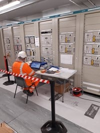 Contractors in PPE sat with a laptop next to a bank of machines.