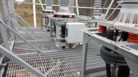 View from inside an elevated metal structure with grated walls and floor. Transmission infrastructure is present within the structure.