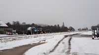 A tractor attached to a trailer with a large cable drum on a snowy road.