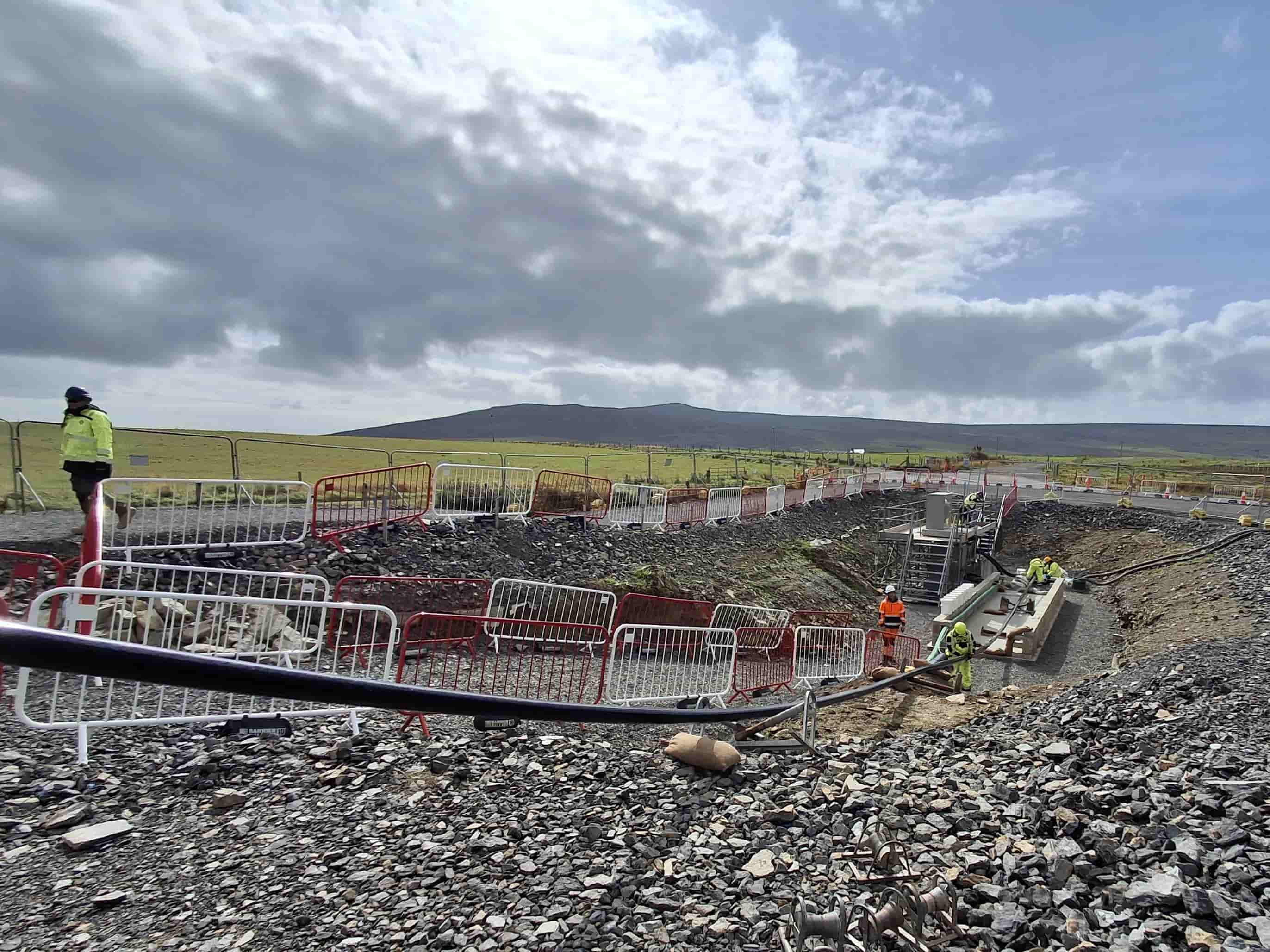 Workers install infrastructure within a fenced excavation on Orkney.