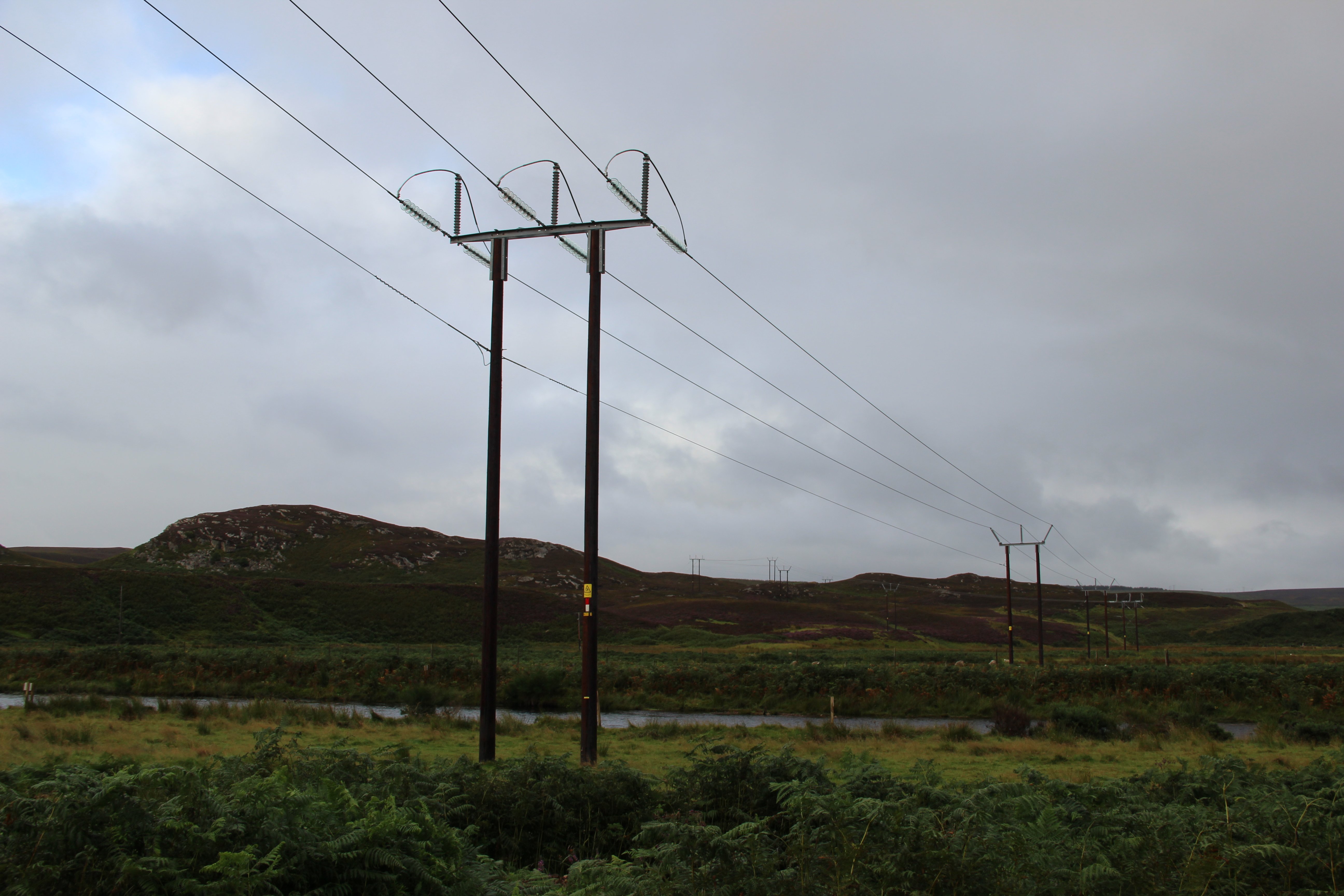 A trident woodpole overheadline stretching across a body of water and over a rocky hill