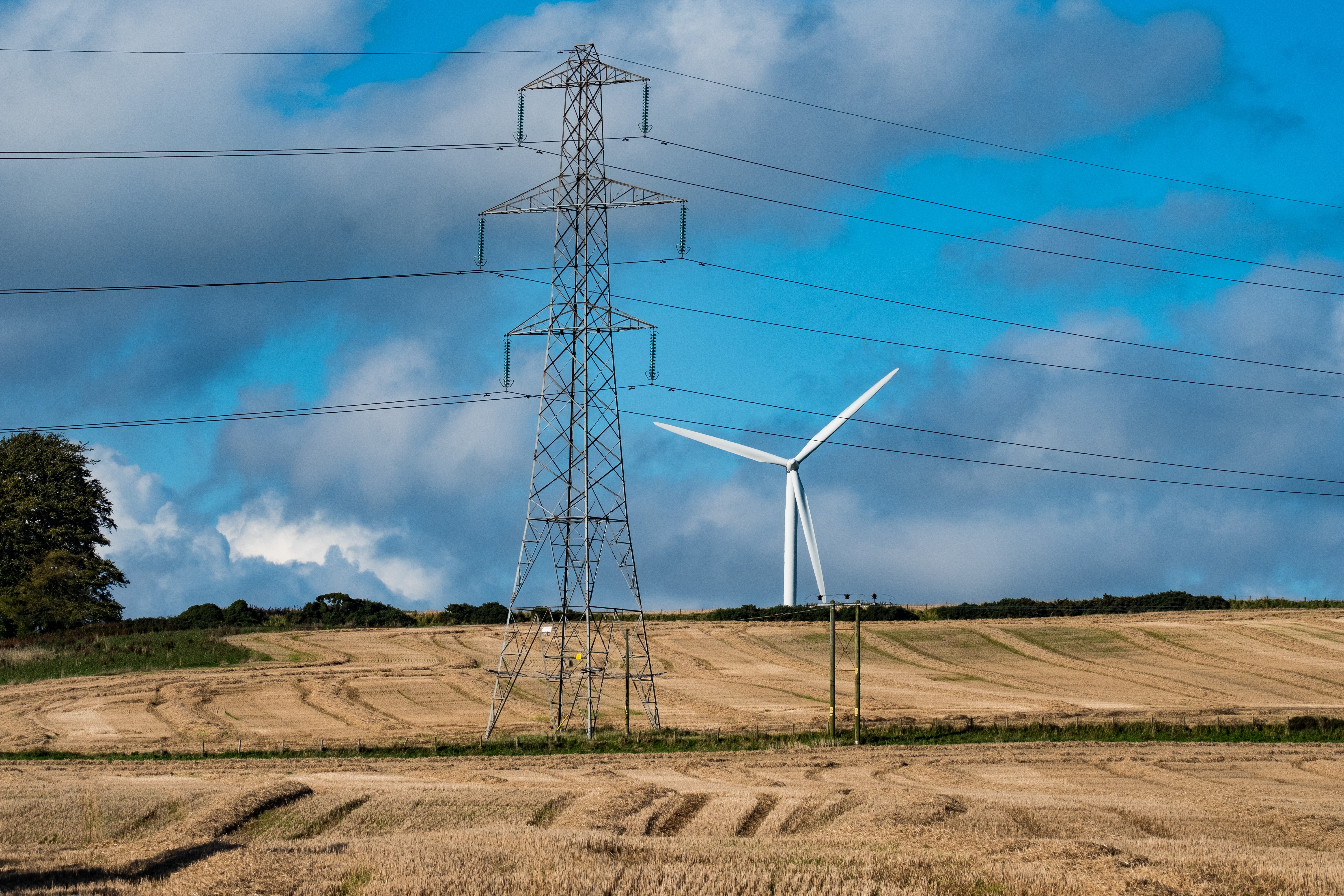 A metal transmission tower, a wind turbine is present behind.