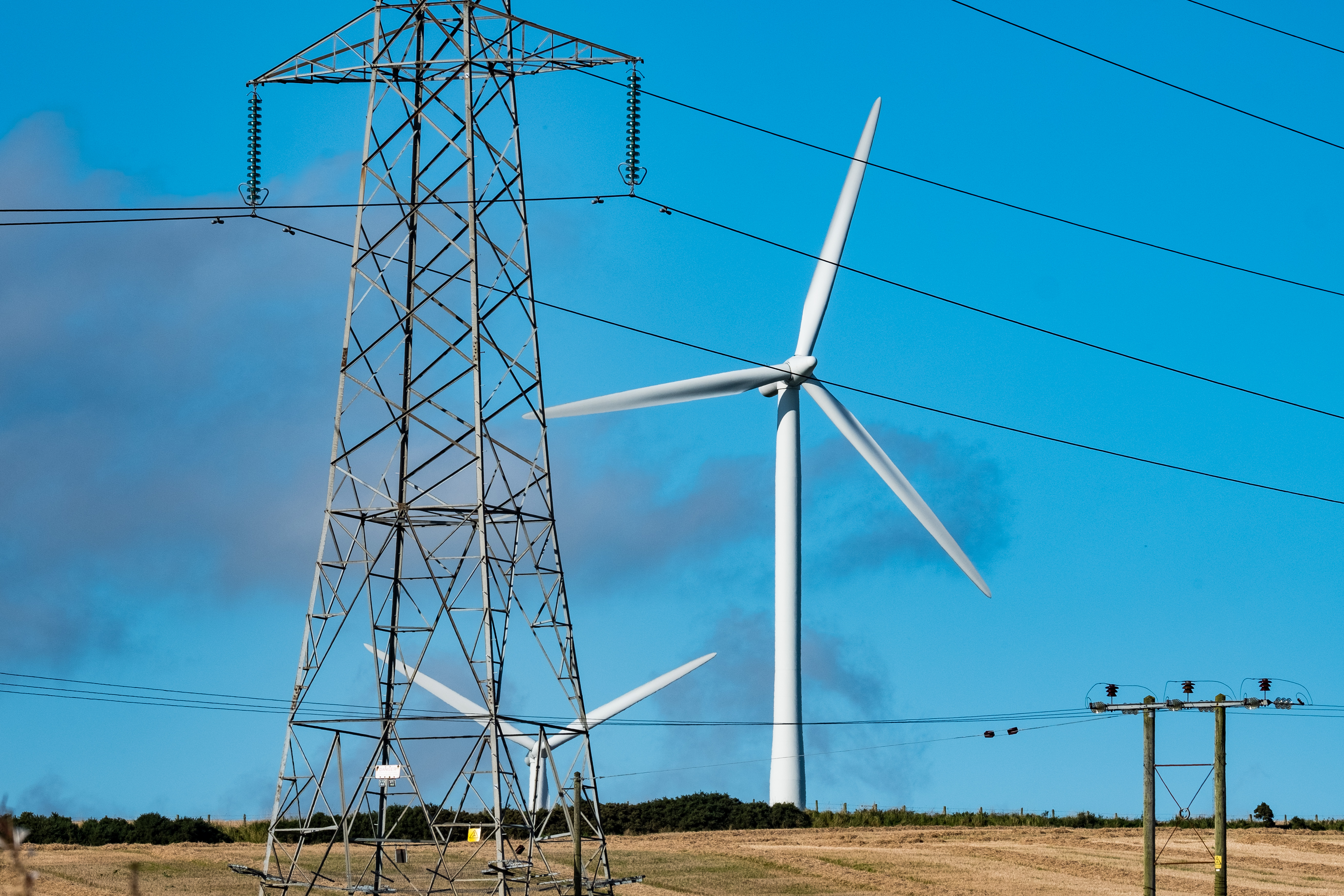 Metal transmission tower with a wind turbine behind it.