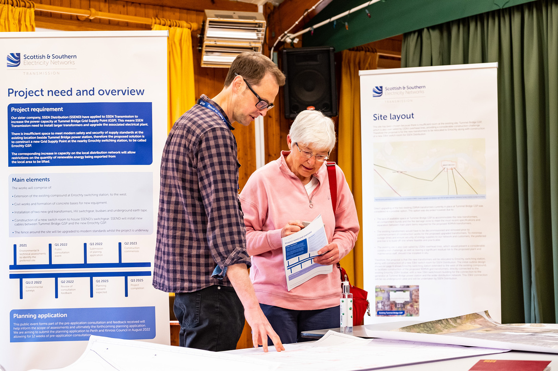 An SSEN Transmission employee and a member of the public examining maps on a table. Project posters are visible behind them.