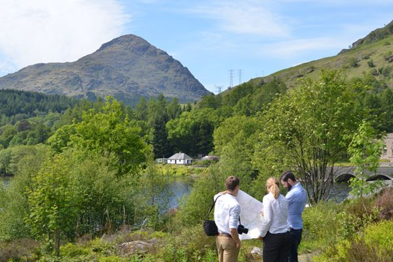 Three people talking in a natural landscape with hills and trees