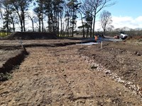 Dirt area of a road under construction, construction vehicles and more surfaced areas are present in the distance.