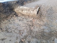 A pipe semi-submerged in dirt, mud and gravel.