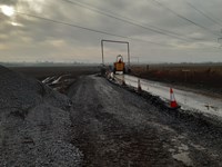 A roughly surfaced road next to a large pile of gravel. A contractor drives a construction vehicle along the road.