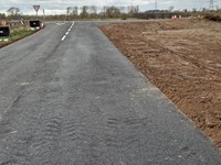 A road leading up to a junction. Wide tire marks are present on the road surface.