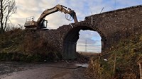 An excavator partially deconstructed stone bridge.