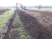 A raised area of loose dirt, an excavator is visible in the distance.