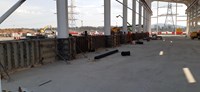 View from inside a metal frame building under construction, construction vehicles and  metal transmission towers in the background.