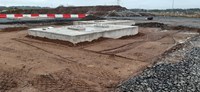 A dirt area with two concrete slabs. Metal fittings extend out of the concrete.