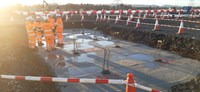 Several contractors in PPE standing on a concrete surface at the base of an excavated area. Metal rebar sticks up in clusters from the concrete.