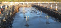 A concrete surface at the base of an excavated area. Metal rebar sticks up in clusters from the concrete.