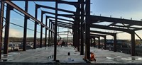 A metal framed building under construction, a contractor in PPE kneels at the base of the structure.