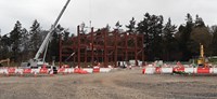 A metal framed building under construction using a crane on a construction site.