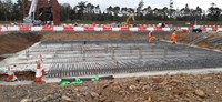 An excavated area, concrete covers the floor and is overlaid by a metal lattice structure.