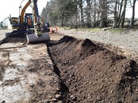 An excavated area with a dirt pile on one side. Contractors in PPE operating an excavator.