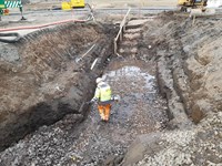 A contractor in PPE at the bottom of an excavated area. A staircase is cut into the earth walls.