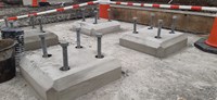 Large threaded metal cylinders topped with a large nut emerge from concrete slabs set into a concrete surface.