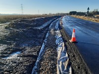 A partially grave-filled trench next to a surfaced road.