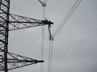 Contractors in PPE atop the arm of a metal transmission tower.