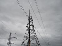 A crane adding a section of a new transmission tower. Several people in PPE are perched on the top of the tower.