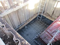 A metal walled excavated area.  Wet concrete covers a metal lattice at the bottom of the hole.