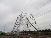 Contractors in PPE atop a base section of a transmission tower under construction.