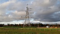 A horizontal platform suspended from the arm of a metal transmission tower. Contractors in PPE stand atop the platform.