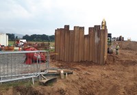 A wall of upright metal sections embedded in the ground of a construction site.