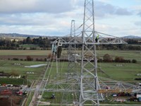 Contractors in PPE atop a metal transmission tower, the tower is partially connected forming a partial overhead line. A date in the corner states "2021/11/03 11:07."