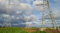 Metal transmission towers forming an overhead line. Contractors in PPE stand atop a gantry suspended from a tower's arm.