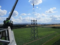 A section of metal transmission tower suspended from a cable.